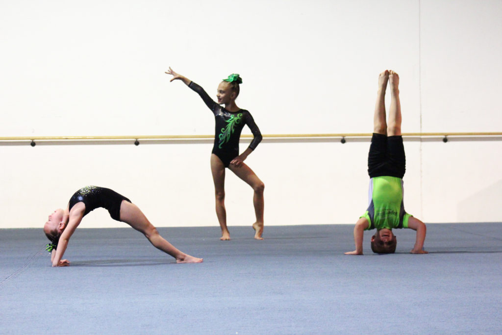 Three young gymnasts doing different positions on the floor.