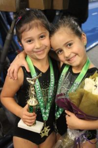Two young girls holding a trophy and flowers.