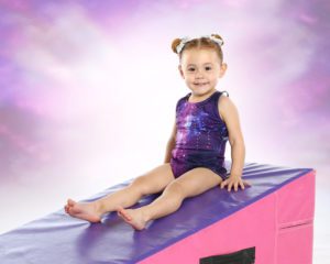 A little girl sitting on top of a pink and purple mat.