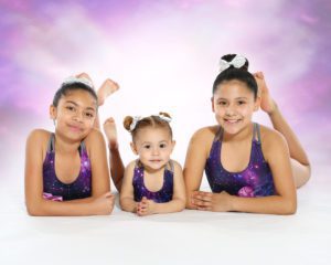 Three young girls posing for a picture in their gymnastics uniforms.