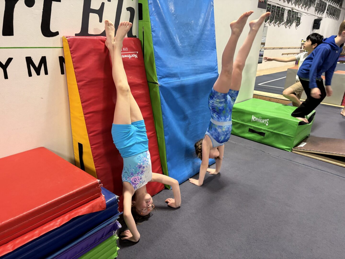 Two children doing handstands against gym wall