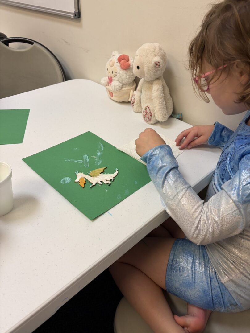 Child crafting on green paper with plush toys